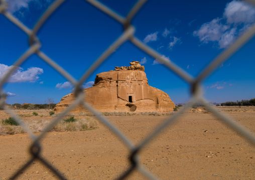 Nabataean tomb in madain saleh archaeologic site seen thru a fence, Al Madinah Province, Al-Ula, Saudi Arabia
