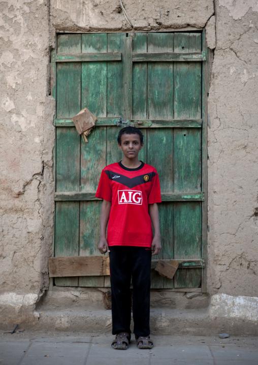 Saudi boy standing in front of an old door, Najran Province, Najran, Saudi Arabia