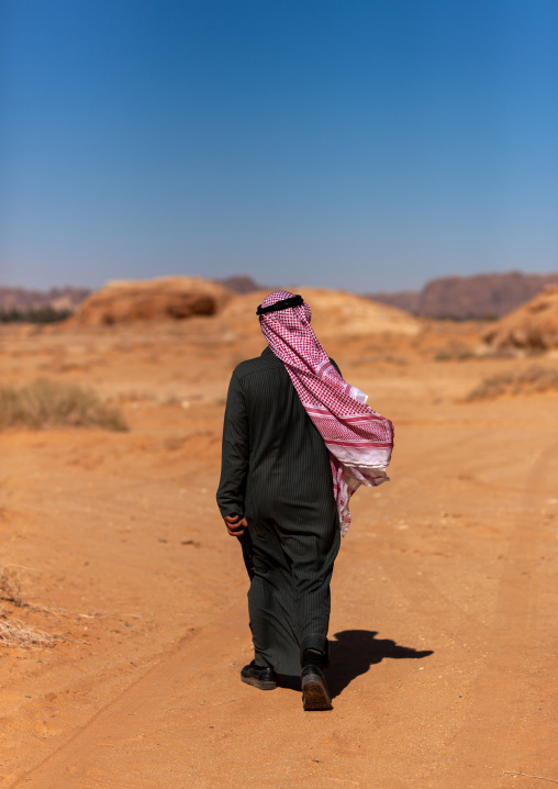 Rear view of a saudi man walking in the desert, Al Madinah Province, Al-Ula, Saudi Arabia