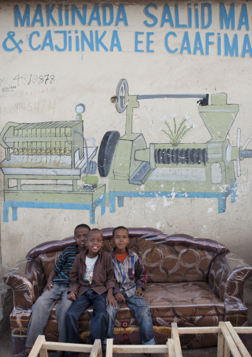 Three Children Sitting In Sofa Underneath A Bilboard Advertisement For A Factory, Hargeisa, Somaliland
