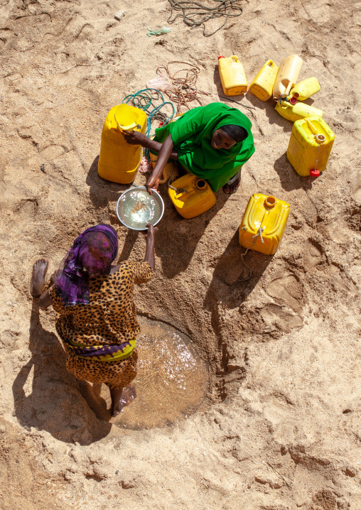 Somali women taking drinking water from a well hole in the sand and pouring it into plastic containers, North-Western province, Lasadacwo Village, Somaliland