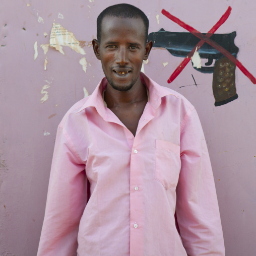 Young Adult In A Pink Shirt Standing Against A Wall With A Weapon Prohibition Sign Painted Onto The Wall, Burao, Somaliland