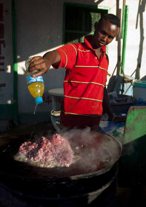 Young Man Wearing A Red Shirt Cooking Red Meat Outdoors, Boorama, Somaliland