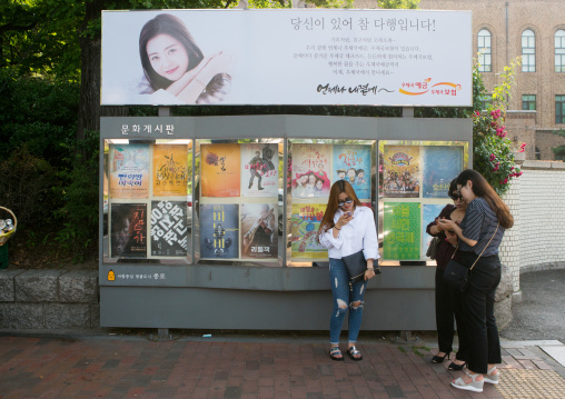Women texting on their mobile phones in front of movie poster in the street, National capital area, Seoul, South korea