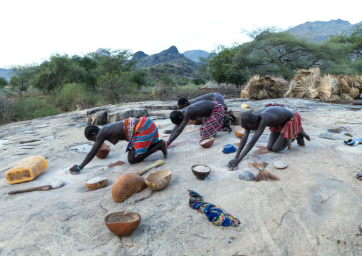 Larim tribe women grinding Sorghum grains in holes in a rock, Boya Mountains, Imatong, South Sudan