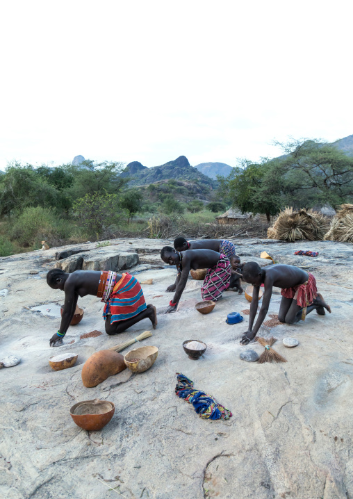 Larim tribe women grinding Sorghum grains in holes in a rock, Boya Mountains, Imatong, South Sudan