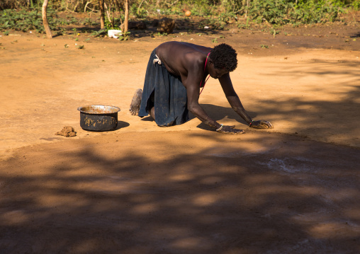 Larim tribe woman making a clean courtyard in front of her hut, Boya Mountains, Imatong, South Sudan