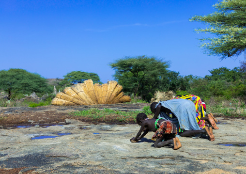 Larim tribe girls grinding sorghum grains in holes in a rock, Boya Mountains, Imatong, South Sudan