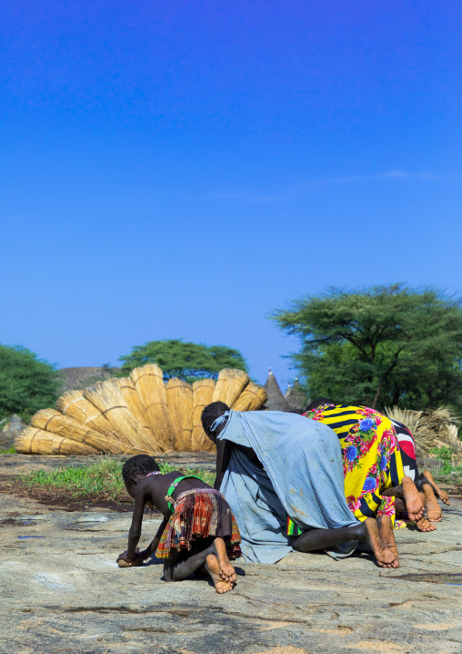 Larim tribe girls grinding Sorghum grains in holes in a rock, Boya Mountains, Imatong, South Sudan
