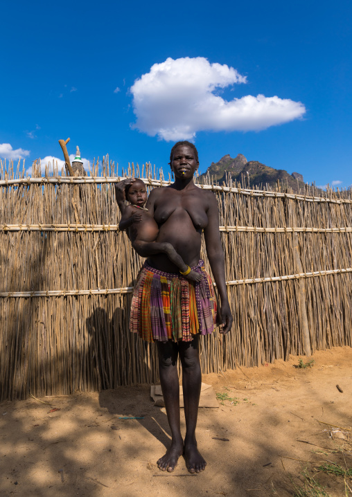 Larim tribe woman carrying her baby in front of a fence, Boya Mountains, Imatong, South Sudan