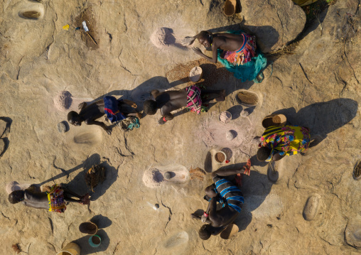 Larim tribe women grinding sorghum grains in holes in a rock, Boya Mountains, Imatong, South Sudan