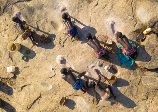 Larim tribe women grinding sorghum grains in holes in a rock, Boya Mountains, Imatong, South Sudan