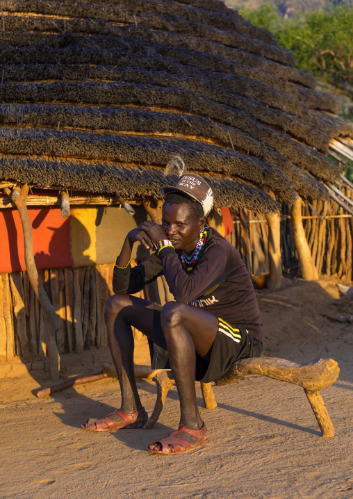 Man sit on a wooden bench in front of a Larim tribe traditional house, Boya Mountains, Imatong, South Sudan