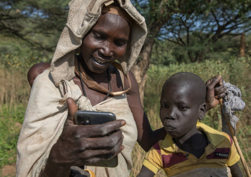 Mourning Larim tribe woman showing a mobile phone to her son, Boya Mountains, Imatong, South Sudan