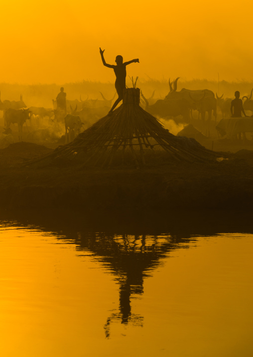 A Mundari tribe boy on a hut roof mimics the position of horns of his favourite cow, Central Equatoria, Terekeka, South Sudan