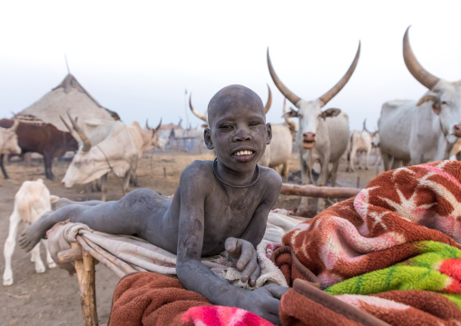 Smiling Mundari tribe boy covered in ash resting on a bed in a cattle camp, Central Equatoria, Terekeka, South Sudan