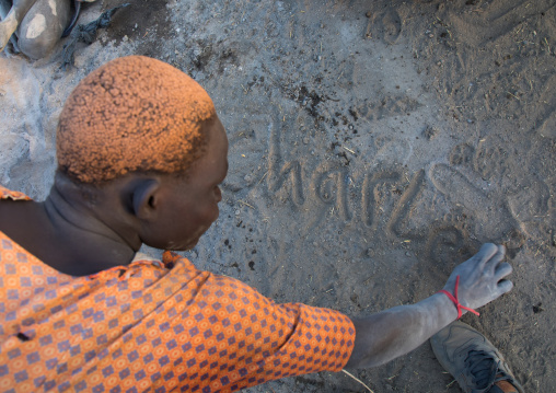 Mundari tribe man with hair dyed in orange with cow urine writing his name in the ashes, Central Equatoria, Terekeka, South Sudan