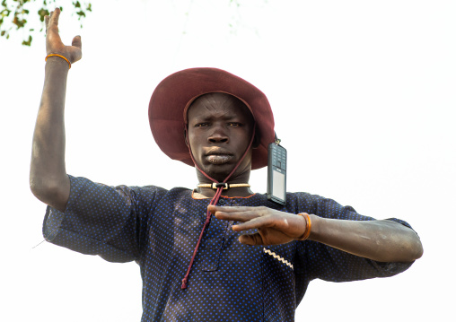 A Mundari tribe man with a mobile phone mimics the position of horns of his favourite cow, Central Equatoria, Terekeka, South Sudan