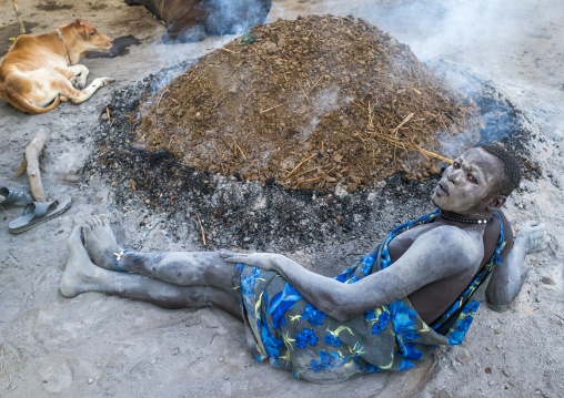 Mundari tribe man resting in front of a bonfire made with dried cow dungs to repel mosquitoes, Central Equatoria, Terekeka, South Sudan