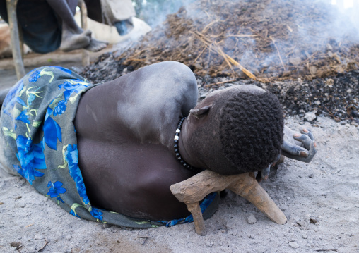 Mundari tribe man resting on a wooden pillow in front of a bonfire made with dried cow dungs to repel mosquitoes, Central Equatoria, Terekeka, South Sudan