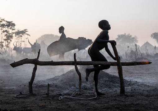 Mundari tribe boy taking care of the bonfires made with dried cow dungs to repel mosquitoes and flies, Central Equatoria, Terekeka, South Sudan