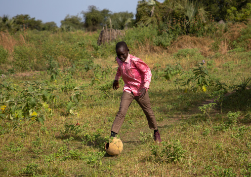 Mundari boy dressed with western clothes plays football before going to sunday mass, Central Equatoria, Terekeka, South Sudan