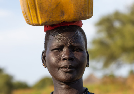 Portrait of a Mundari tribe woman with scarifications on the forehead carrying a jerrican, Central Equatoria, Terekeka, South Sudan