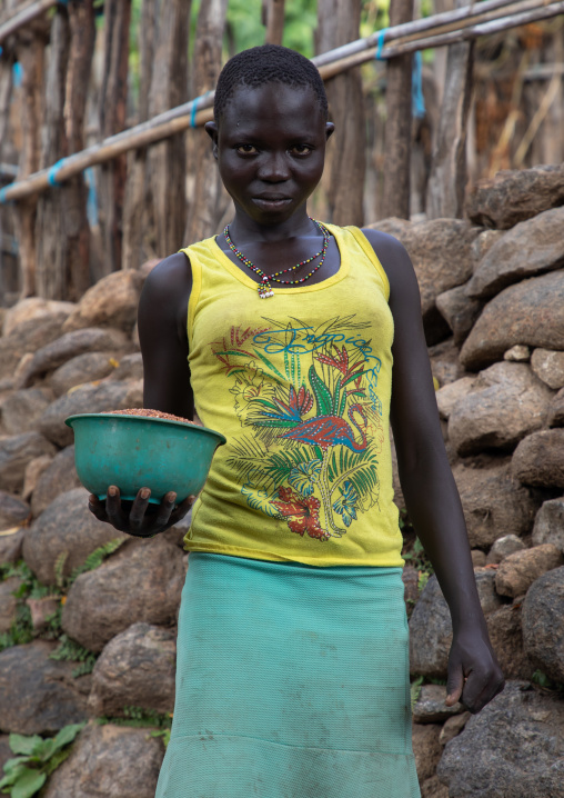 Lotuko tribe woman carrying food in front of a stone wall, Central Equatoria, Illeu, South Sudan