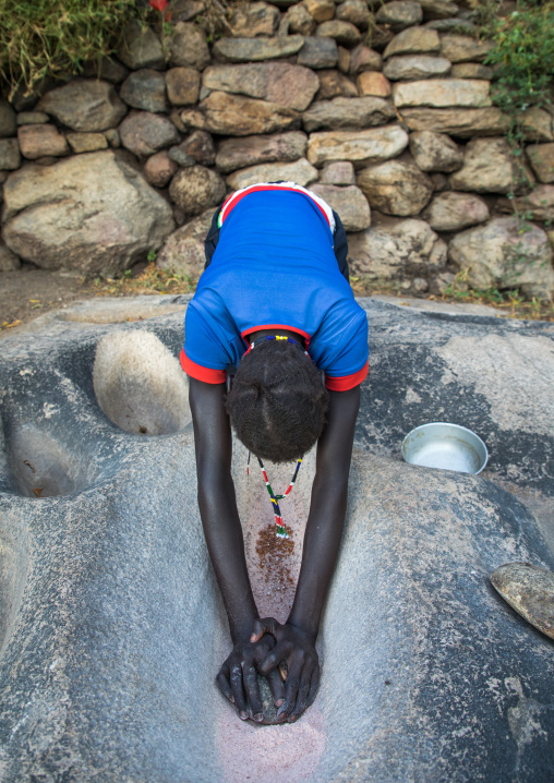 Lotuko tribe woman grinding grains in a hole in the rock, Central Equatoria, Illeu, South Sudan