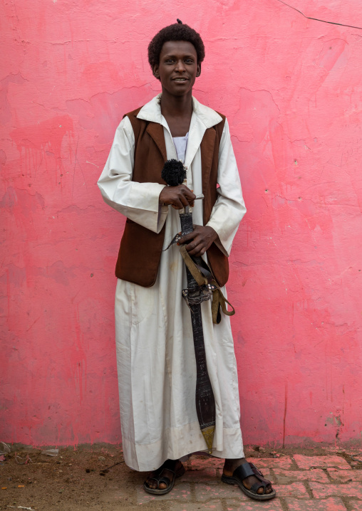 Beja tribe warrior with his sword in front of a pink wall, Red Sea State, Port Sudan, Sudan