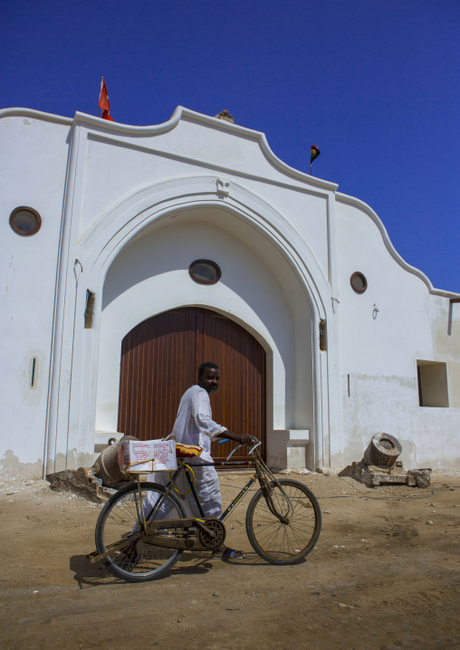 Sudan, Port Sudan, Suakin, man passing with his bicycle in front of the renovated building of the gateway to customs