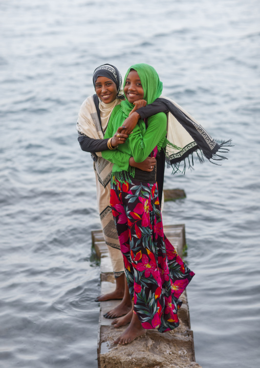 Sudan, Port Sudan, Suakin, girls standing on a rock on the red sea bank