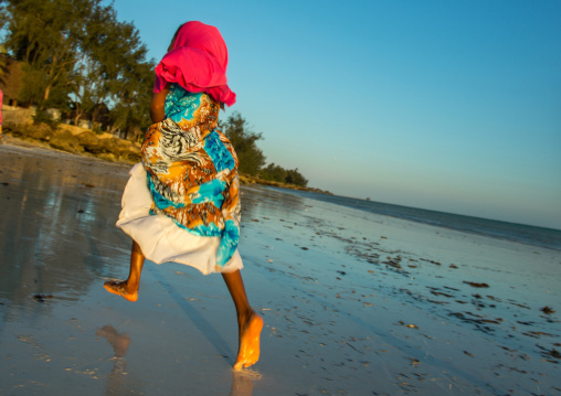 Tanzania, Zanzibar, Kizimkazi, young muslim girl in school uniform running on beach