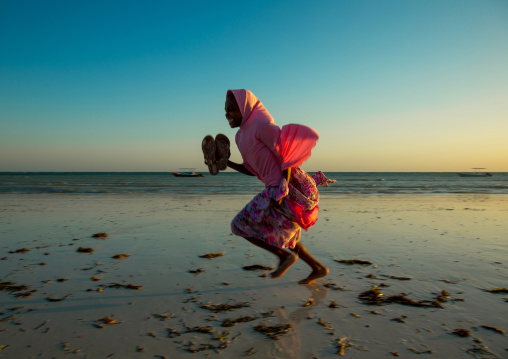 Tanzania, Zanzibar, Kizimkazi, young muslim girl in school uniform running on beach