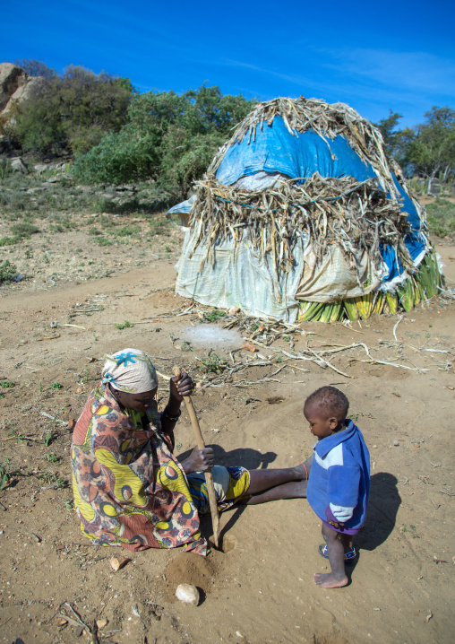 Tanzania, Serengeti Plateau, Lake Eyasi, hadzabe tribe woman with her child building a traditional hut made with sisal agaves