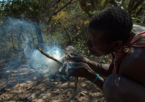 Tanzania, Serengeti Plateau, Lake Eyasi, hadzabe man blowing on twigs to start fire