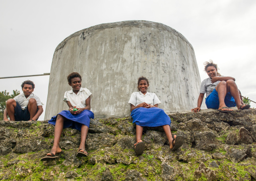 Teenagers in school uniforms sit in front of a concrete water tank, Shefa Province, Efate island, Vanuatu