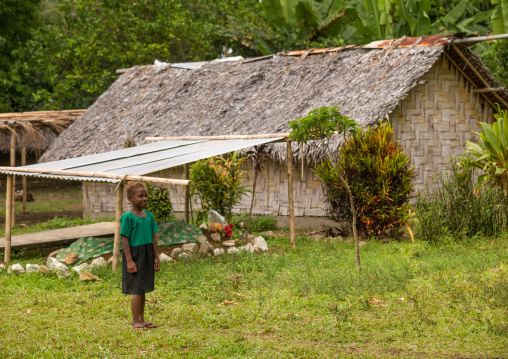 Ni-Vanuatu child in front of a traditional house made with palm leaves and a tomb, Shefa Province, Efate island, Vanuatu