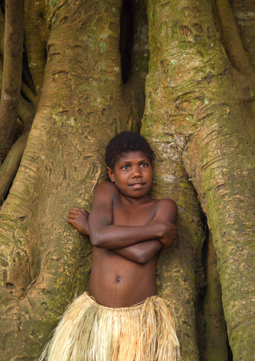 Little girl with a grass skirt standing in front of banyan tree roots, Tanna island, Yakel, Vanuatu