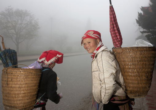 Red dzao women carrying umbrellas in the baskets on their back, Sapa, Vietnam