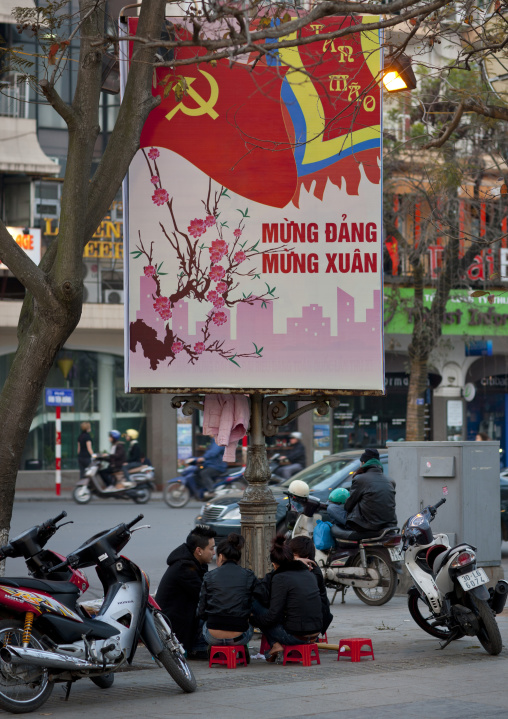 Teenagers sitting under a propaganda panel of the communist party, Hanoi, Vietnam