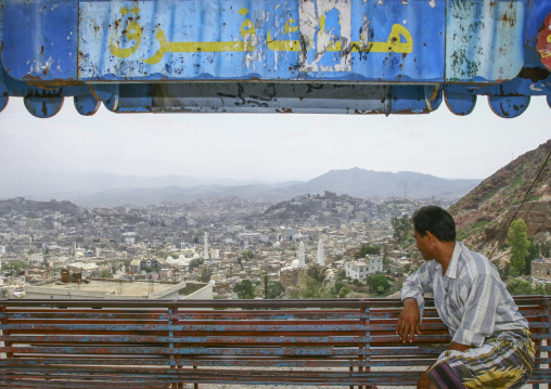 Yemeni man on a bench looking at city from Al-Cahira fortress, Janad Region, Taiz, Yemen