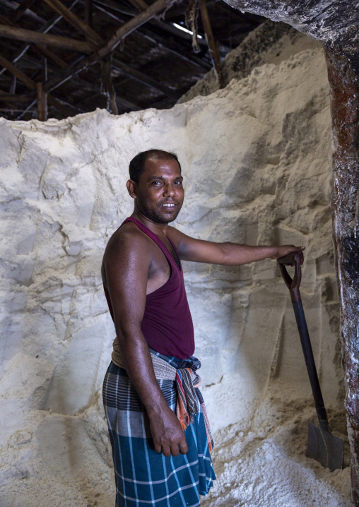 Bangladeshi man picks up salt with a shovel in a warehouse, Chittagong Division, Chittagong, Bangladesh