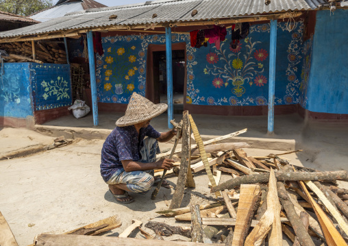 Man cutting wood in front of a traditional wall painting, Rajshahi Division, Tikoil, Bangladesh