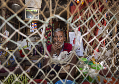 Vendor smoking in a shop protected by a net, Dhaka Division, Dhaka, Bangladesh