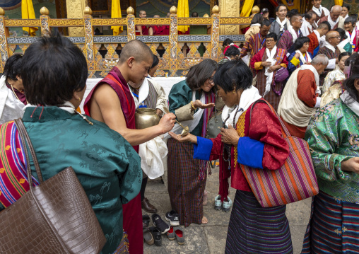 Monk giving black lentils with milk to pilgrims in Punakha dzong, Punakha dzongkhag, Punakha, Bhutan