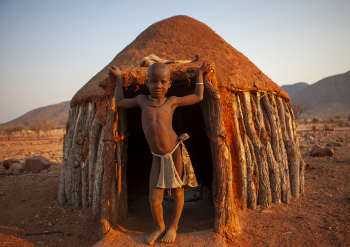 Himba boy in the entrance of his hut, Kunene region, Epupa, Namibia