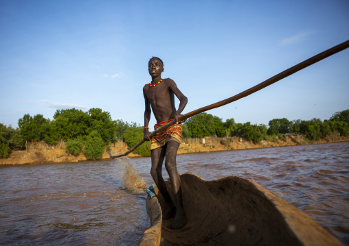 Young boy pushing a boat on the omo river, Omorate, Omo valley, Ethiopia