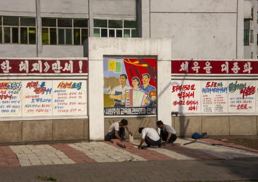North Korean men working in front of propaganda billboard, DGC, Pyongyang, North Korea