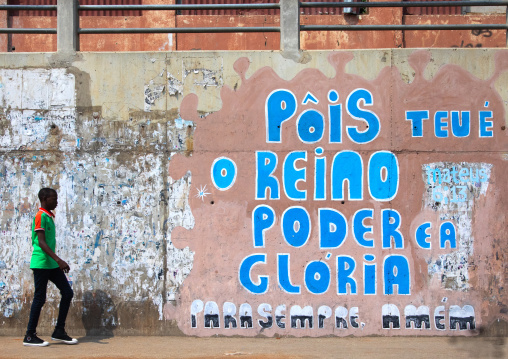 Angolan boy walking in front of a wall covered with graffitis, Luanda Province, Luanda, Angola